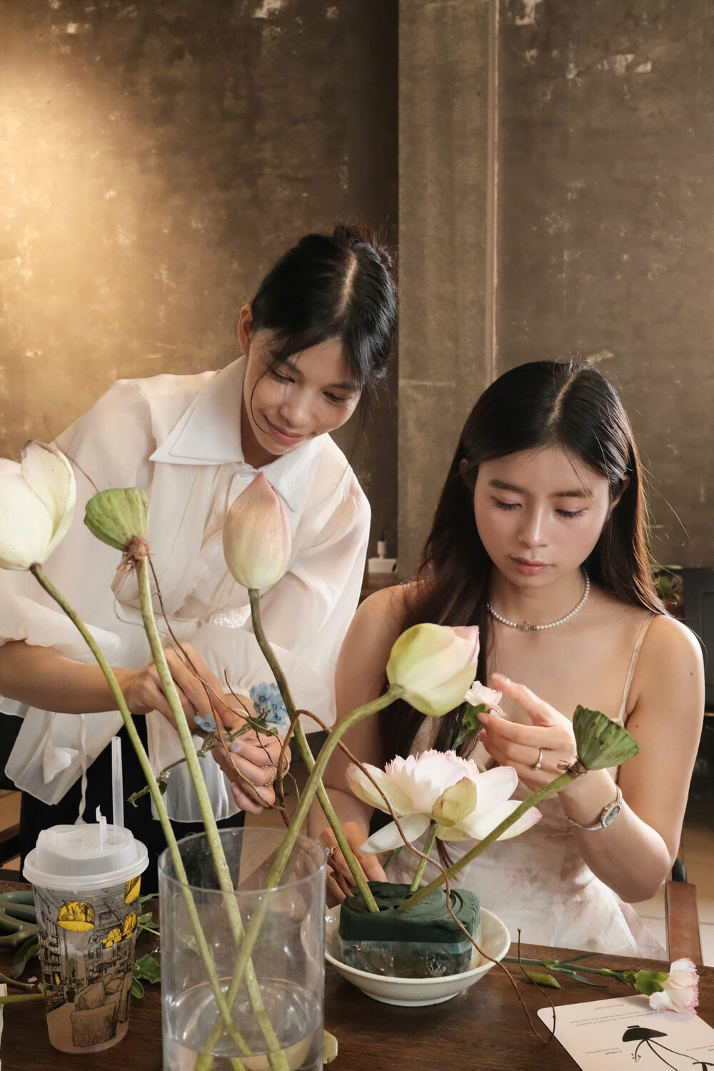 Arranging pink lotus stems with the teacher alongside